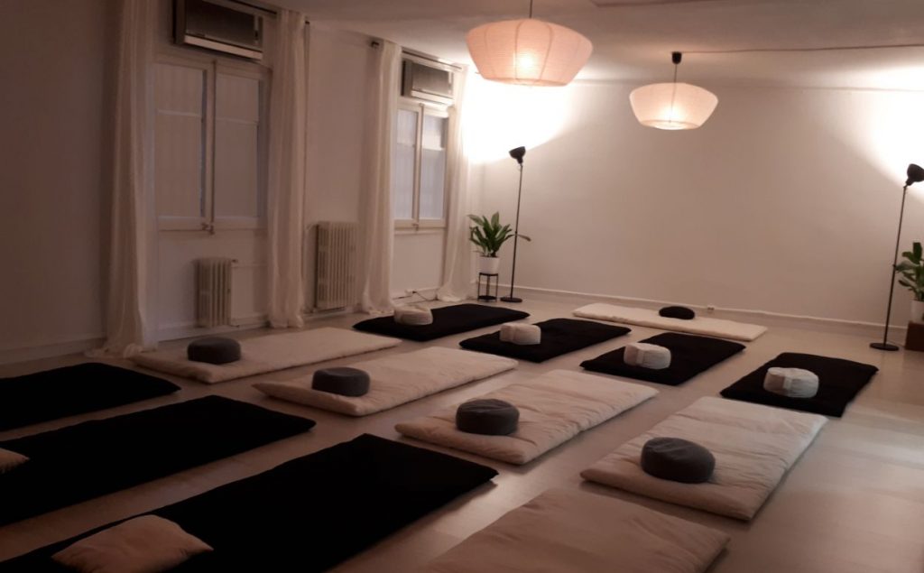 Espai diàfan il·luminat amb llum agradable i suau amb diversos futons a terra preparats per fer pràctica de relaxació profunda.