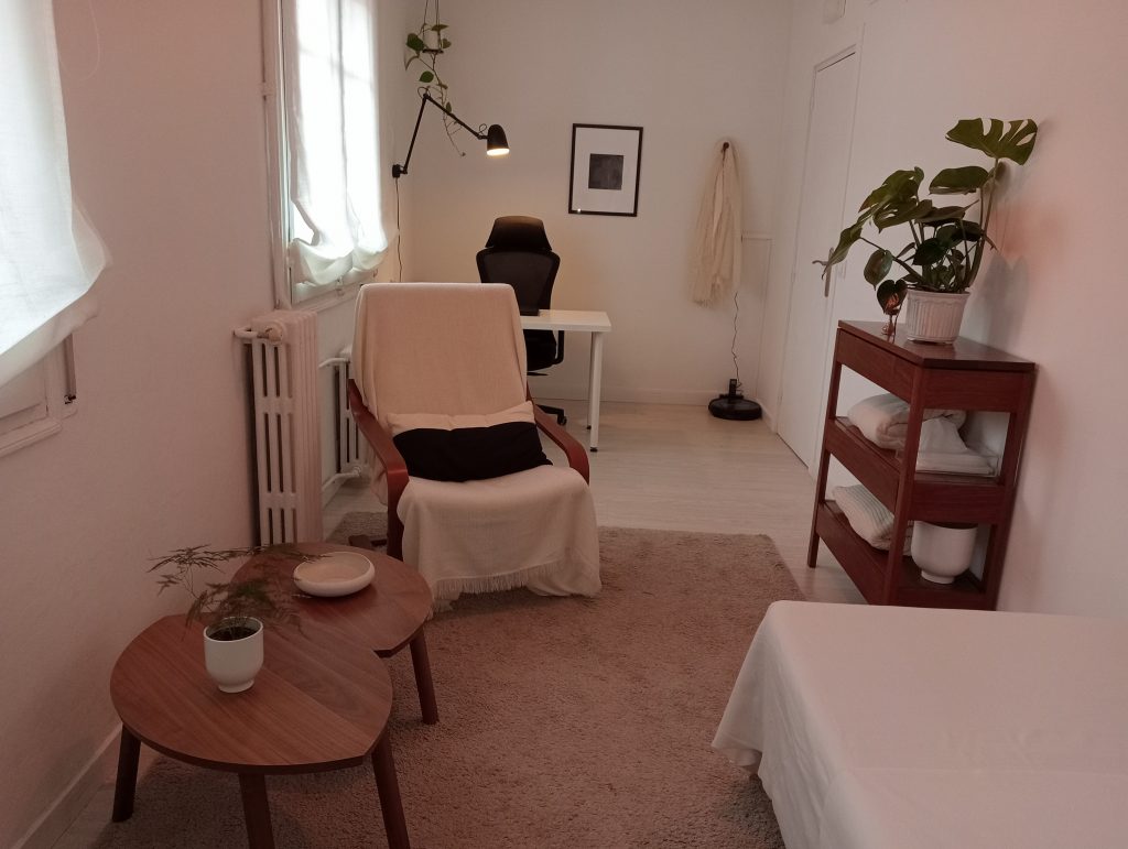 Despacho terapéutico iluminado con luz ténue y equipado con una butaca y un escritorio con mesa y silla, preparado para hacer terapia.