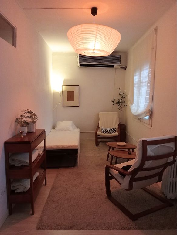 Sala de terapia con un diván y dos sillones, iluminación relajante y decoración en colores neutros.