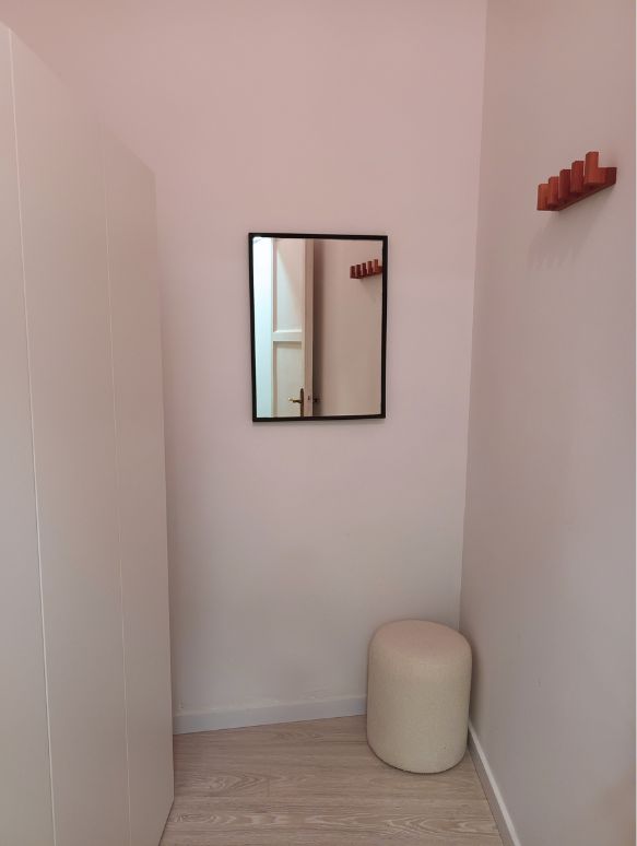 Pequeño espacio con un espejo, una banqueta y un colgador para dejar la ropa.