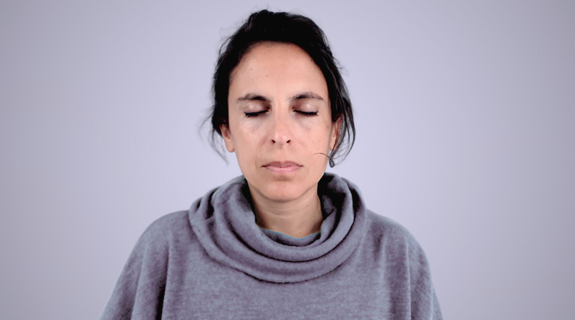 Woman practicing meditation with her eyes closed and dressed with a grey jumper